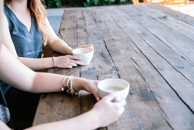 Deux femmes boivent du café à une table en bois.