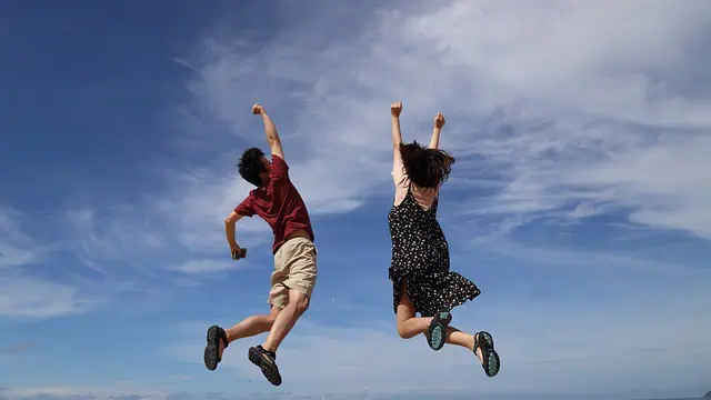 Deux personnes sautant joyeusement dans les airs sur fond de ciel bleu et de nuages épars.